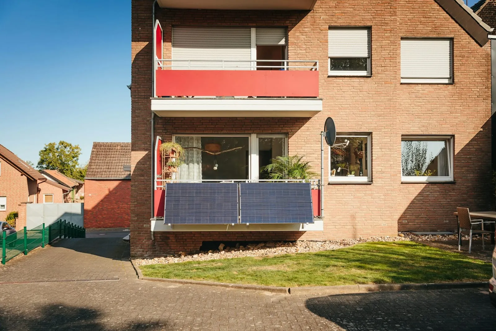 A brick house with two plug-in solar panels fixed to its ground-floor balcony
