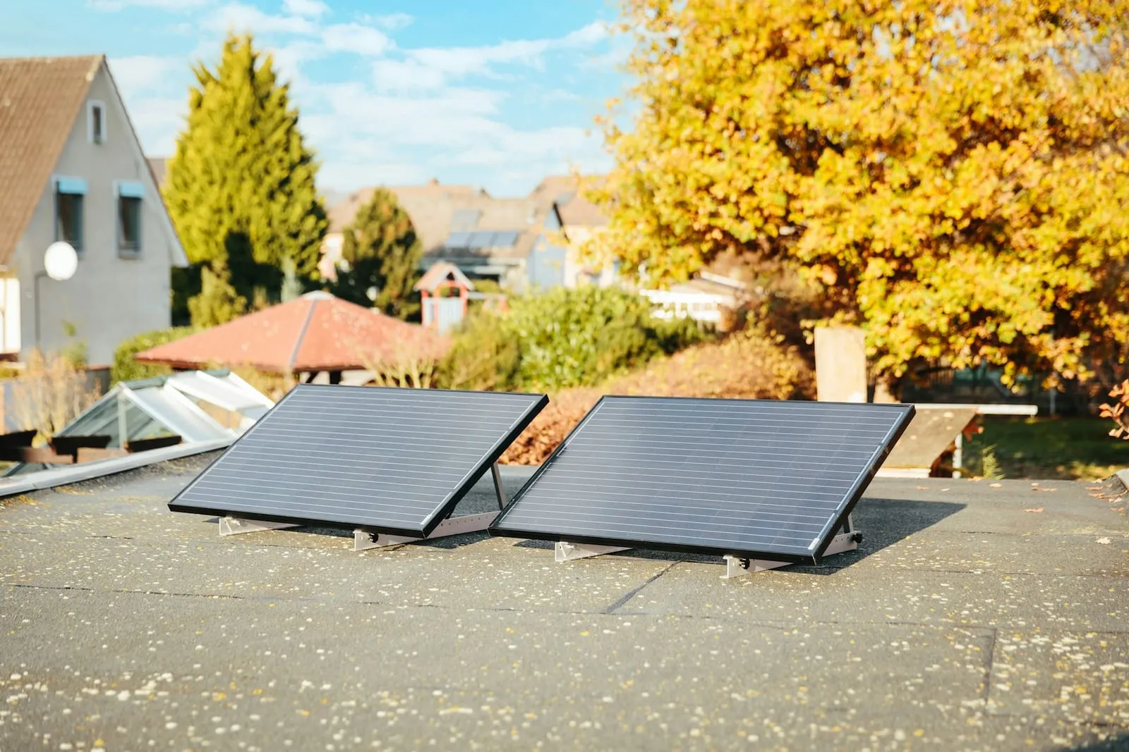Two solar panels on low tilted frames on a flat roof, with autumn trees behind