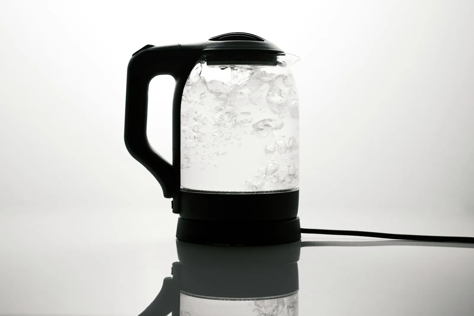 A glass electric kettle full of boiling water on a white worktop