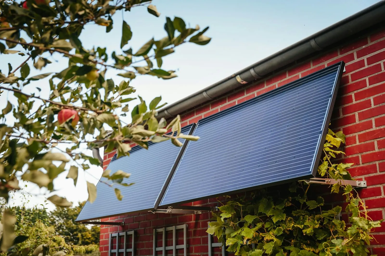 Two solar panels mounted flat against a red-brick wall under the eaves